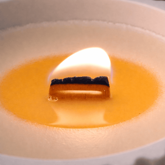 Vela aromática de soja artesanal encendida en cuenco con pabilo de madera y llama cálida
