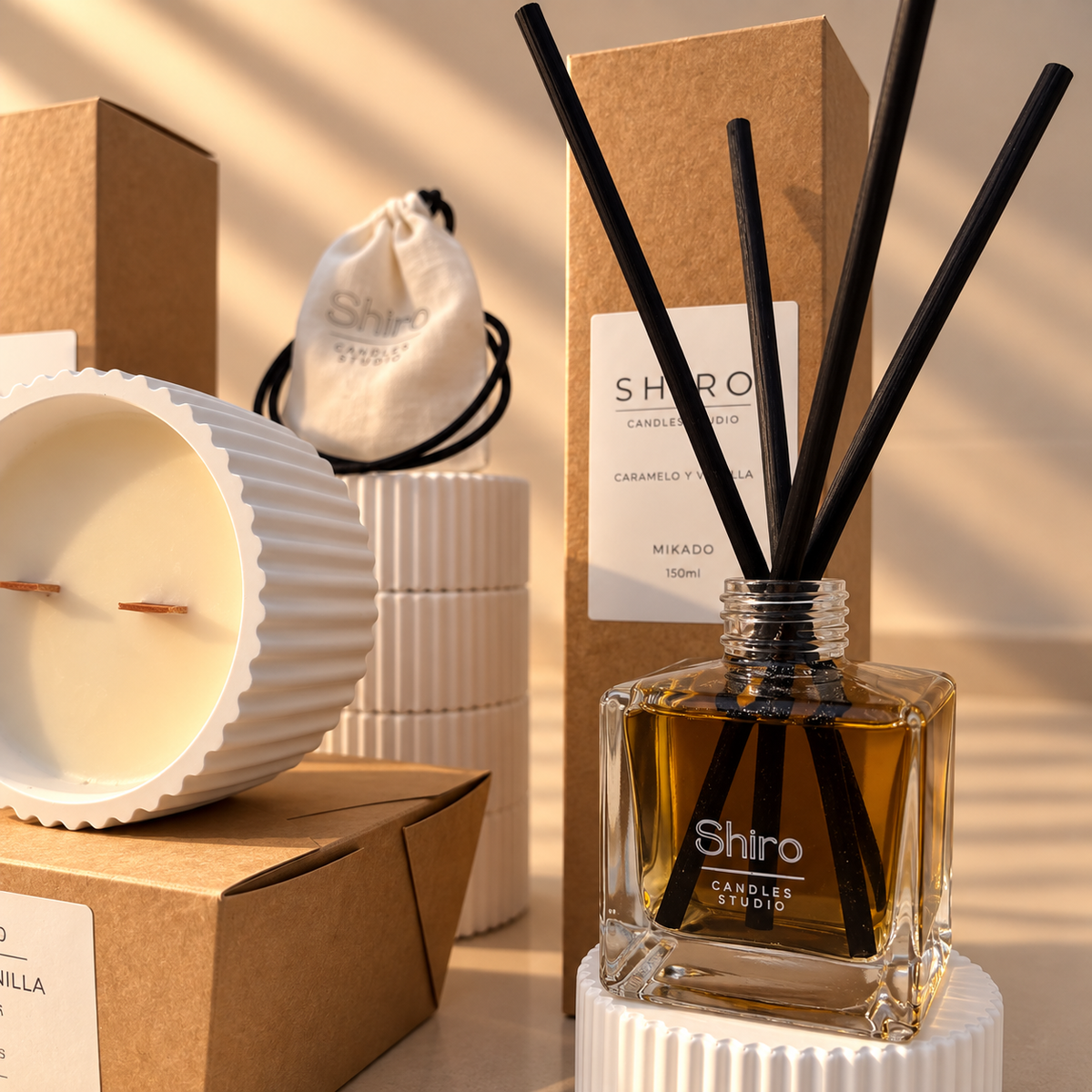 Mikado aromático Caramelo & Vainilla de Shiro Candles Studio, con varillas negras y frasco de cristal de 150 ml, presentado junto a una vela de soja del pack Aroma Total.
