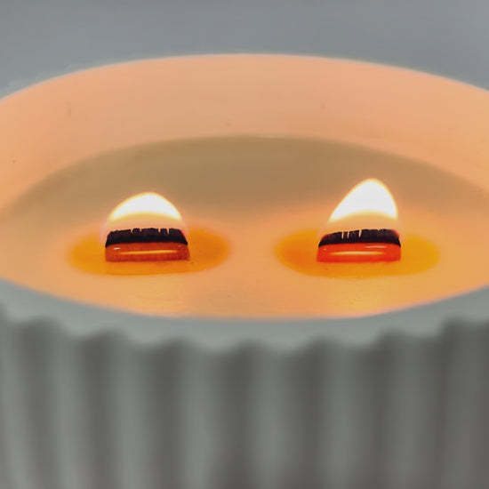 Vela aromática de soja natural encendida con pabilo de madera crepitante en cuenco cerámico artesanal
