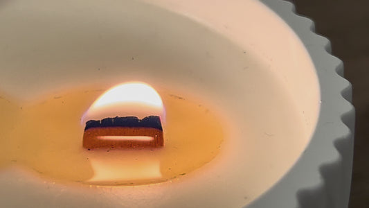 Video detalle de vela aromática de soja encendida con pabilo de madera crepitante y ambiente cálido y acogedor