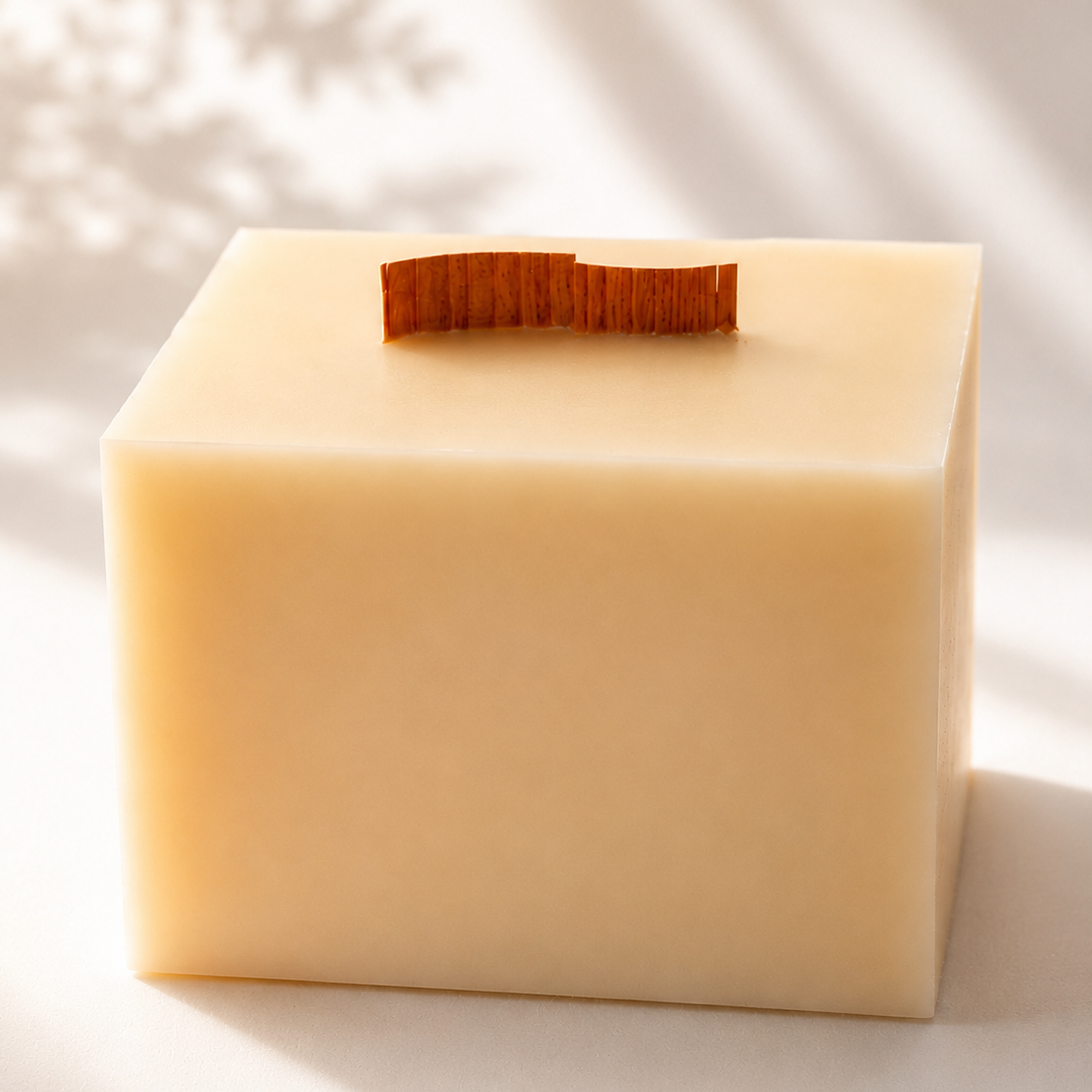 Primer plano de una vela decorativa de cera de soja en forma de cubo con mecha de madera ondulada, perteneciente a la colección Altea de Shiro Candles Studio, sobre un fondo blanco con iluminación cálida