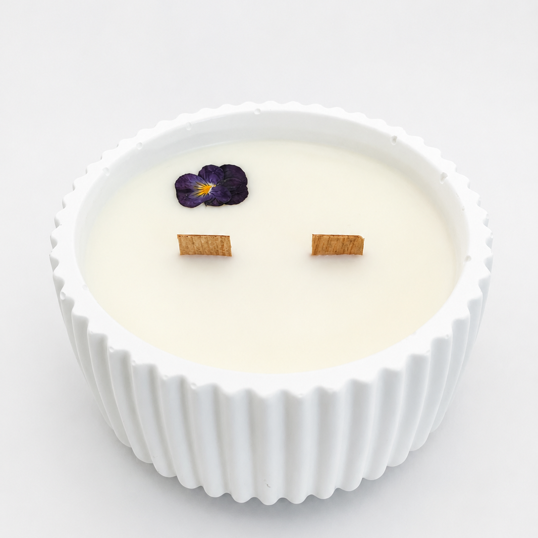 Vela aromática de violeta y vainilla blanca en recipiente blanco de resina ecológica, con doble mecha de madera y flor violeta prensada.
